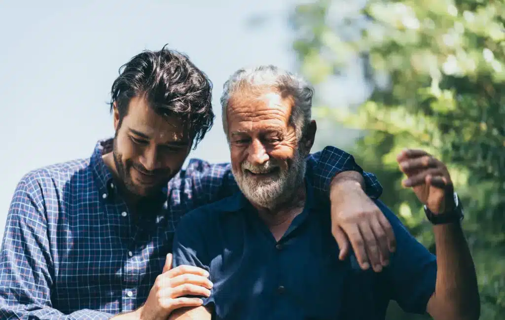 An adult son walks with his arms around his father.