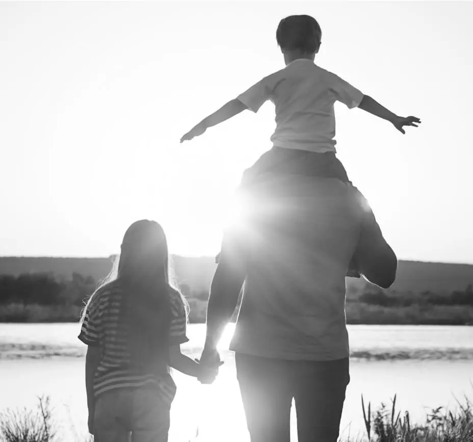 a parent holds the hand of one child while another gets a shoulder ride