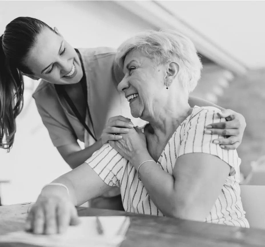 A younger woman smiles with an older woman and holds her hand.