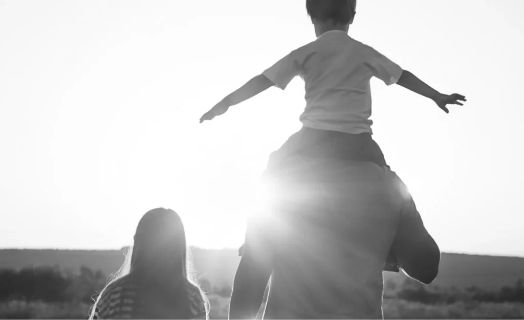 A parent holds the hand of one child while another gets a shoulder ride.